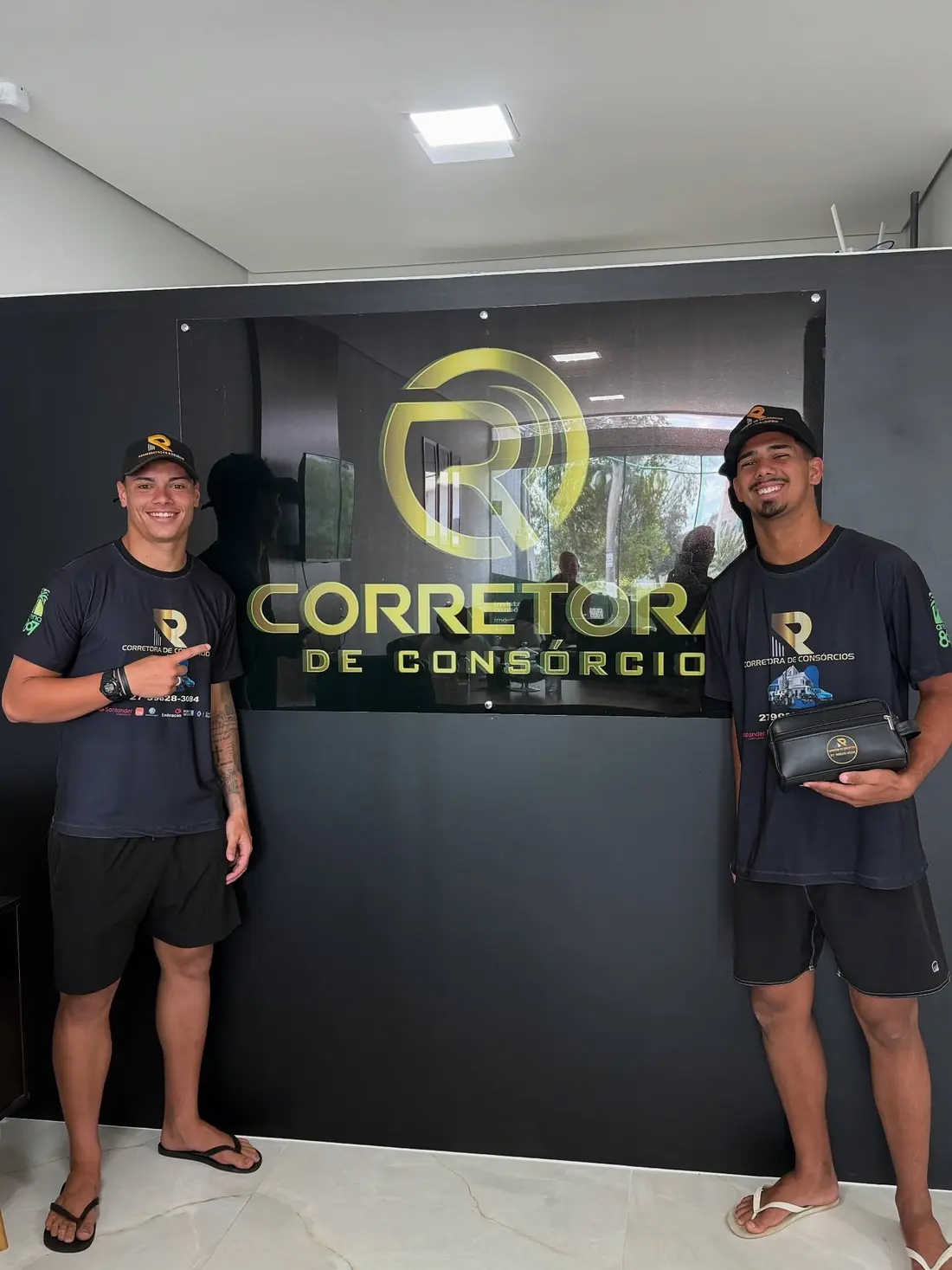 Dois atletas de futevôlei usando uniformes com a marca R Corretora no escritório